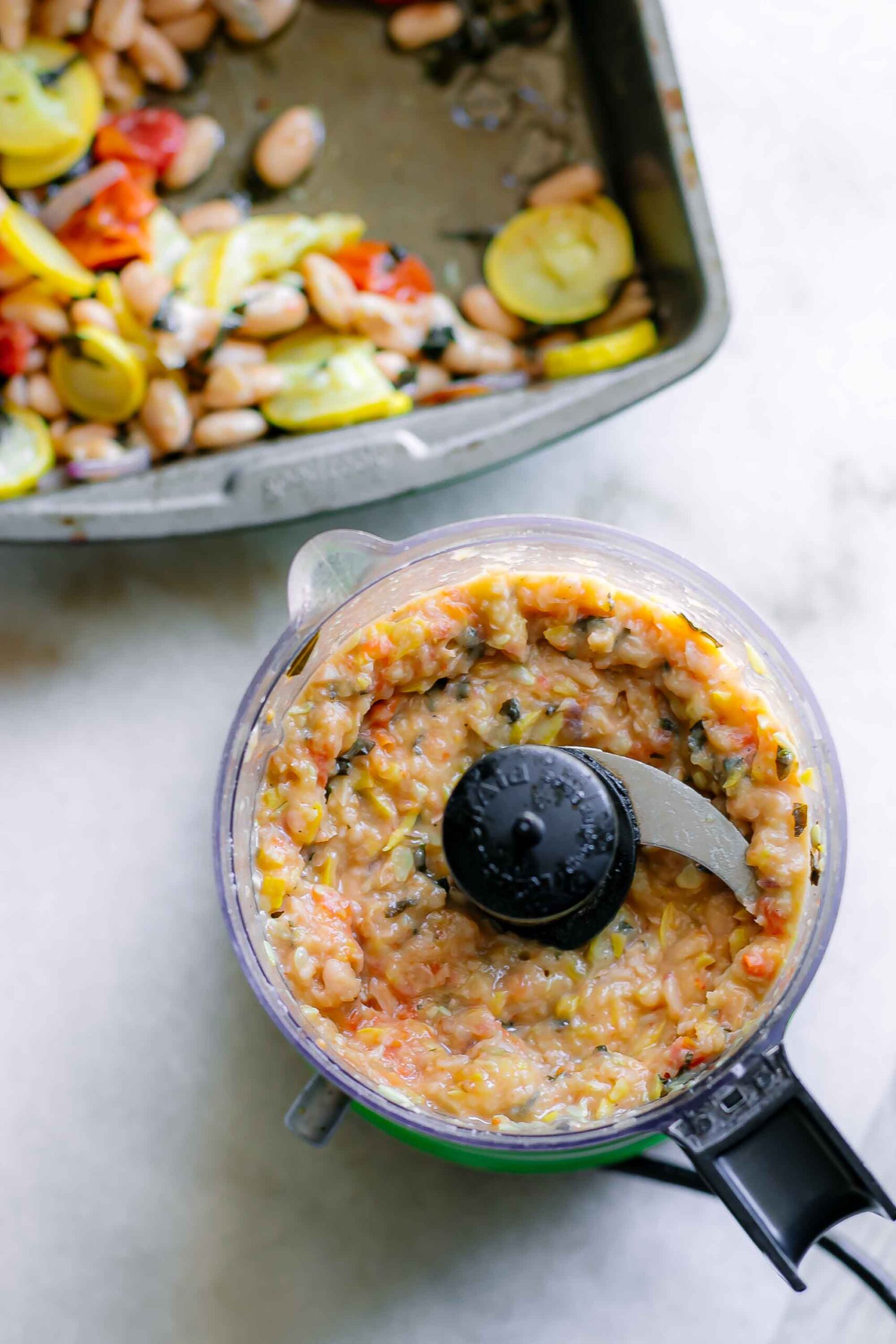 blended vegetable and bean sauce for pasta in a food processor on a table with a pan of roasted vegetables