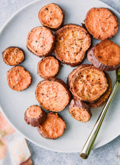 roasted sweet potato rounds on a white plate with a gold fork