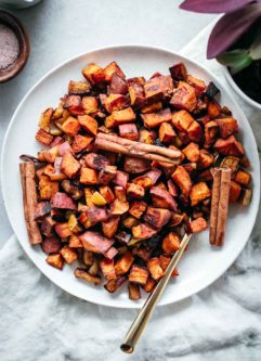 roasted diced sweet potatoes and apples on a white plate with cinnamon sticks