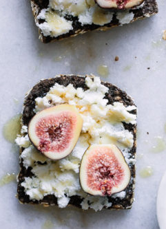 A piece of breakfast bread with cheese, figs, and honey on a table.