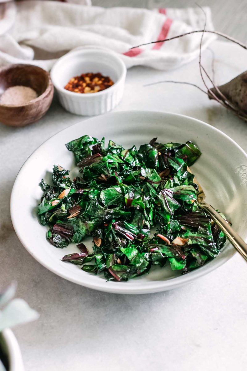 sauteed beet leaves in a white bowl with a gold fork on a white table