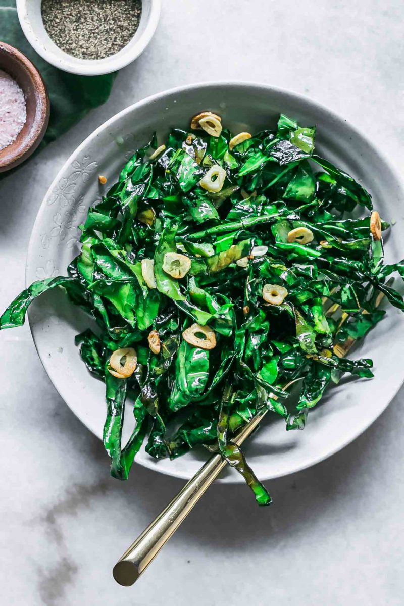 sauteed brussels sprouts greens with garlic in a bowl with a gold fork on a white table