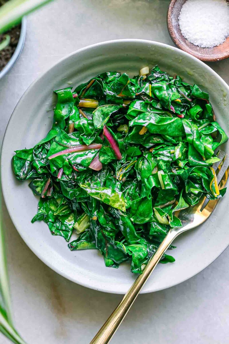 a plate with pan fried chard leaves on a plate with a gold fork