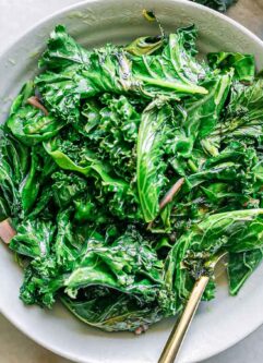 a white bowl with sautéed kale and chard leaves on a white table