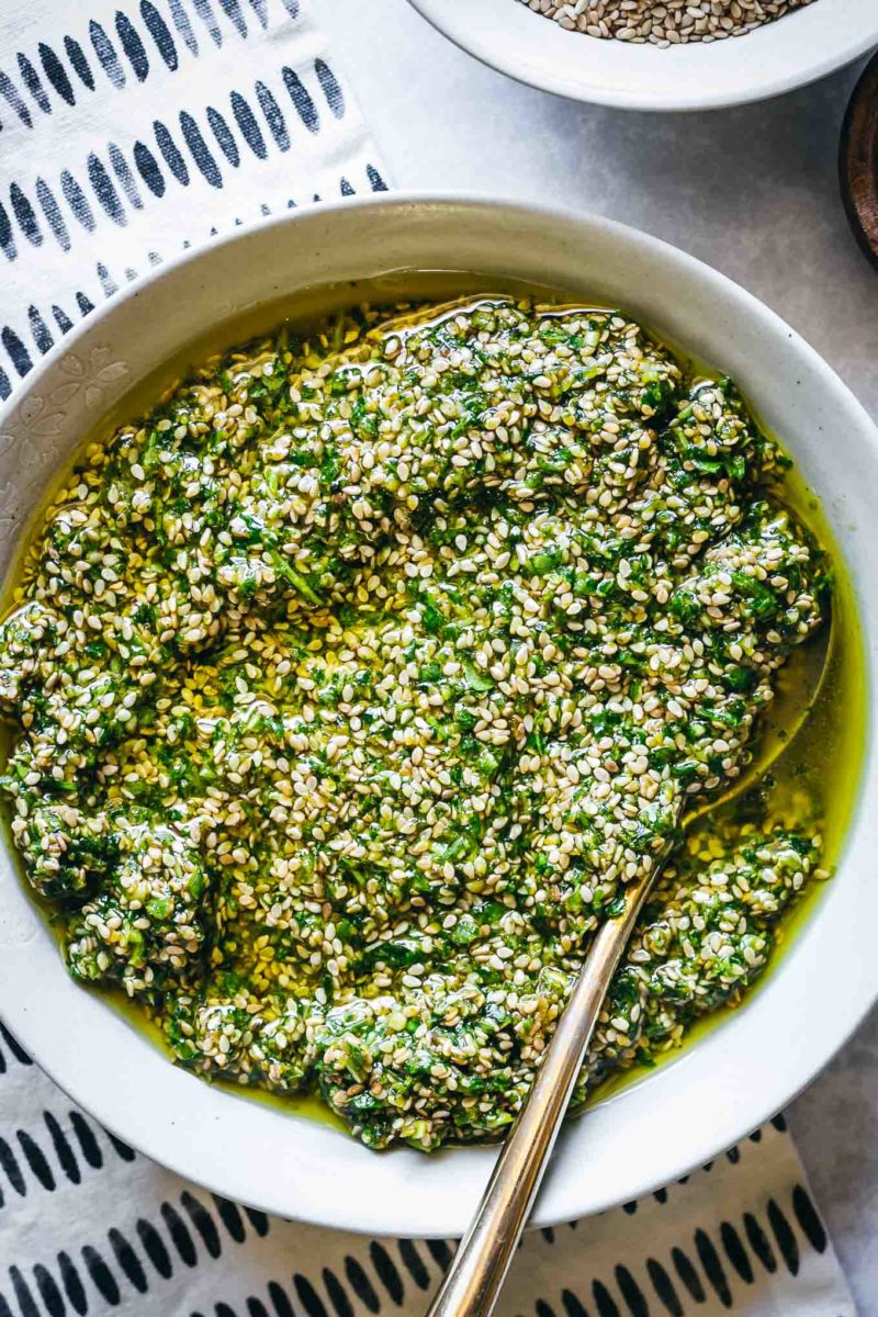 sesame seed pesto in a white bowl with a gold spoon