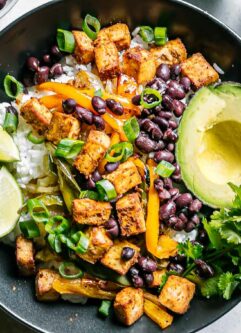 a bowl with a tofu fajita bowl with avocado, limes, and cilantro on a white table