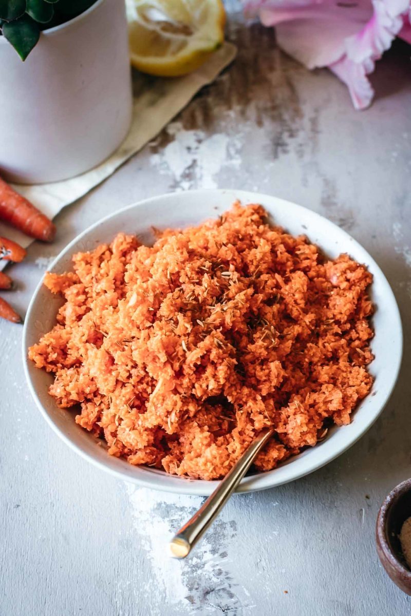 shredded carrots in a while bowl with a gold spoon