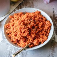 shredded carrot salad in a white bowl with a gold spoon