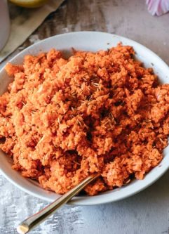 shredded carrot salad in a white bowl with a gold spoon
