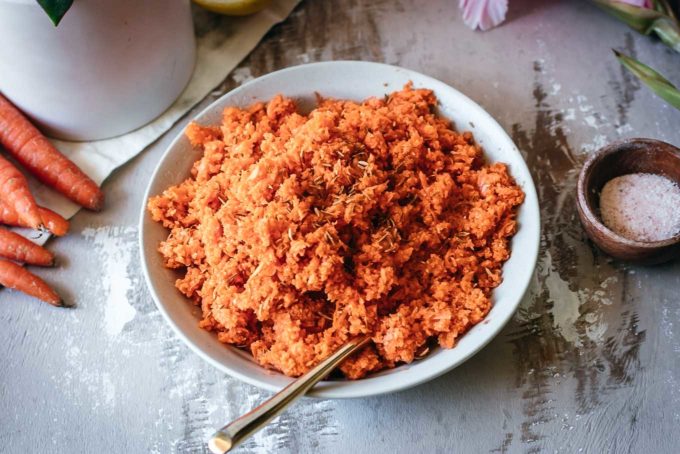 shredded carrot salad in a white bowl with a gold spoon on wood table