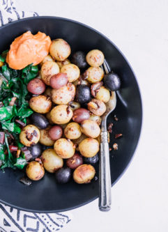 A black bowl with breakfast potatoes, cooked greens, and garlic aioli.
