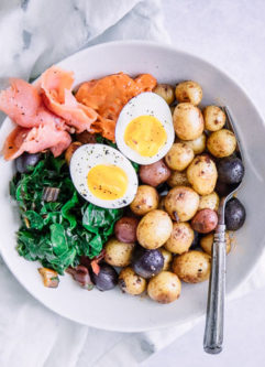 A savory breakfast bowl with salmon, eggs, and potatoes on a white bowl.