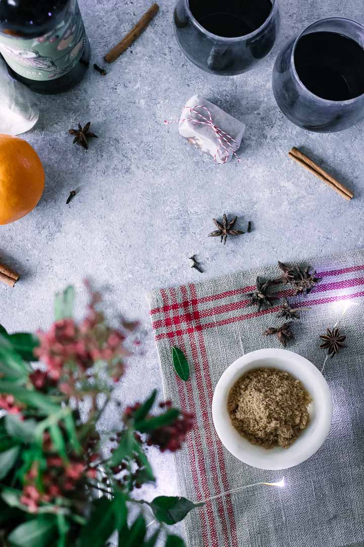 brown sugar, cinnamon, star anise, cloves, oranges, and winter flowers on a blue table
