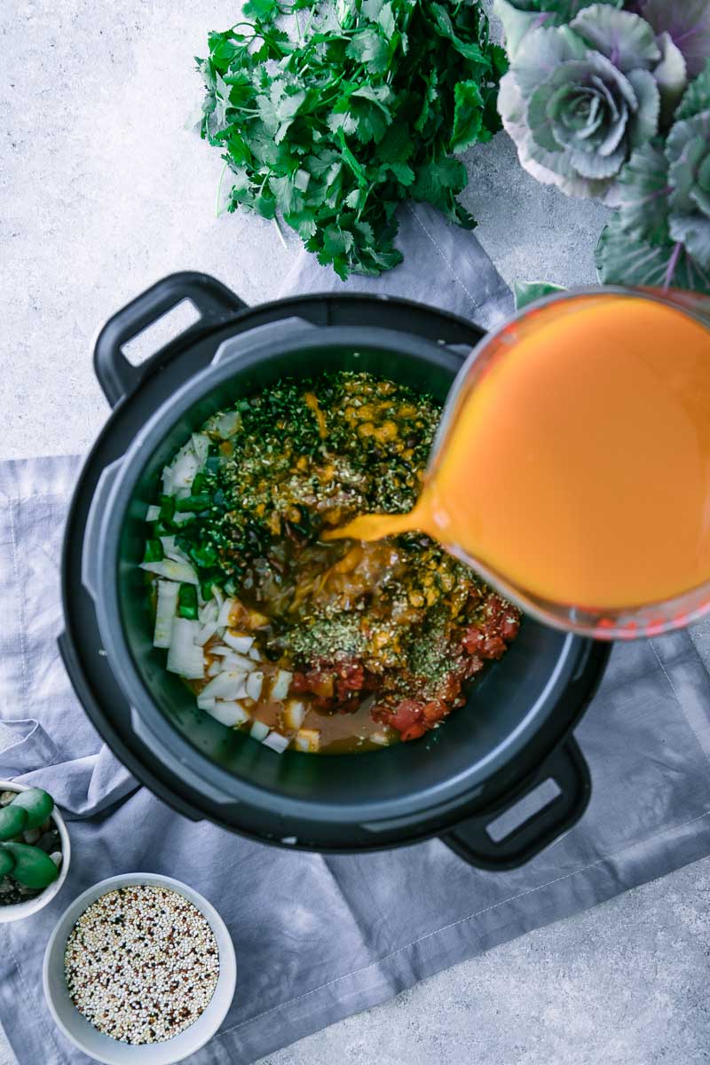 vegetable broth pouring into an instant pot pressure cooker filled with vegetables on a white table