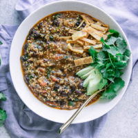 a white bowl of chili made with black beans with avocado, cilantro, and tortillas strips
