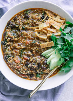 a white bowl of chili made with black beans with avocado, cilantro, and tortillas strips