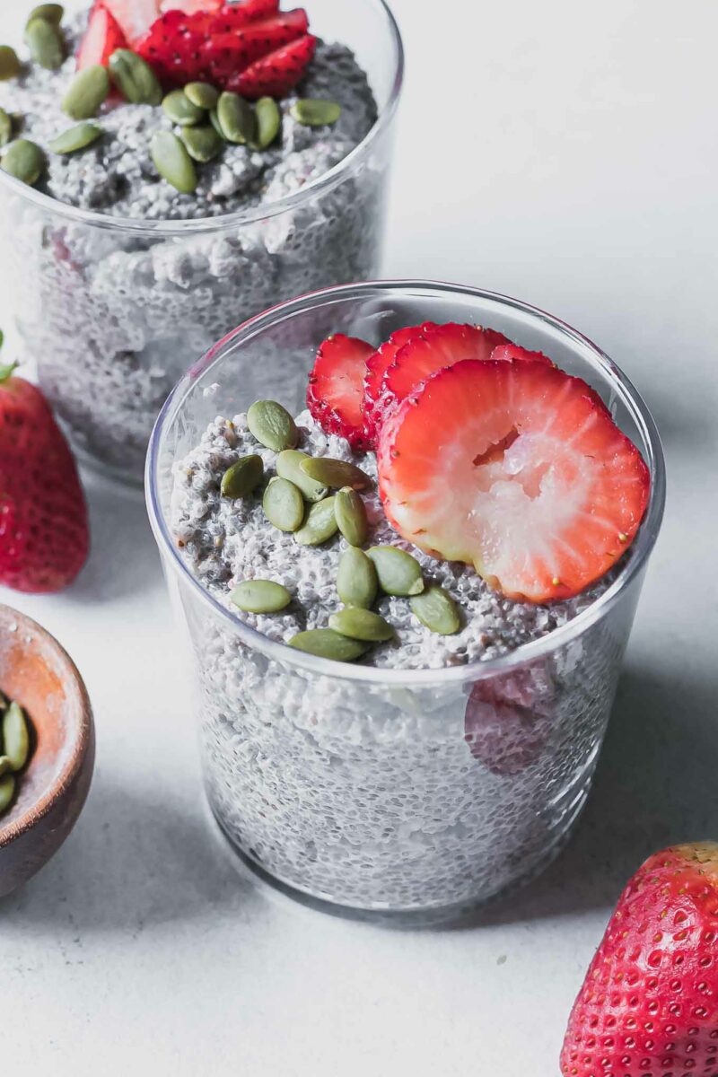 a glass with strawberry chia seed pudding and topped with a sliced strawberry on a white table with fresh strawberries