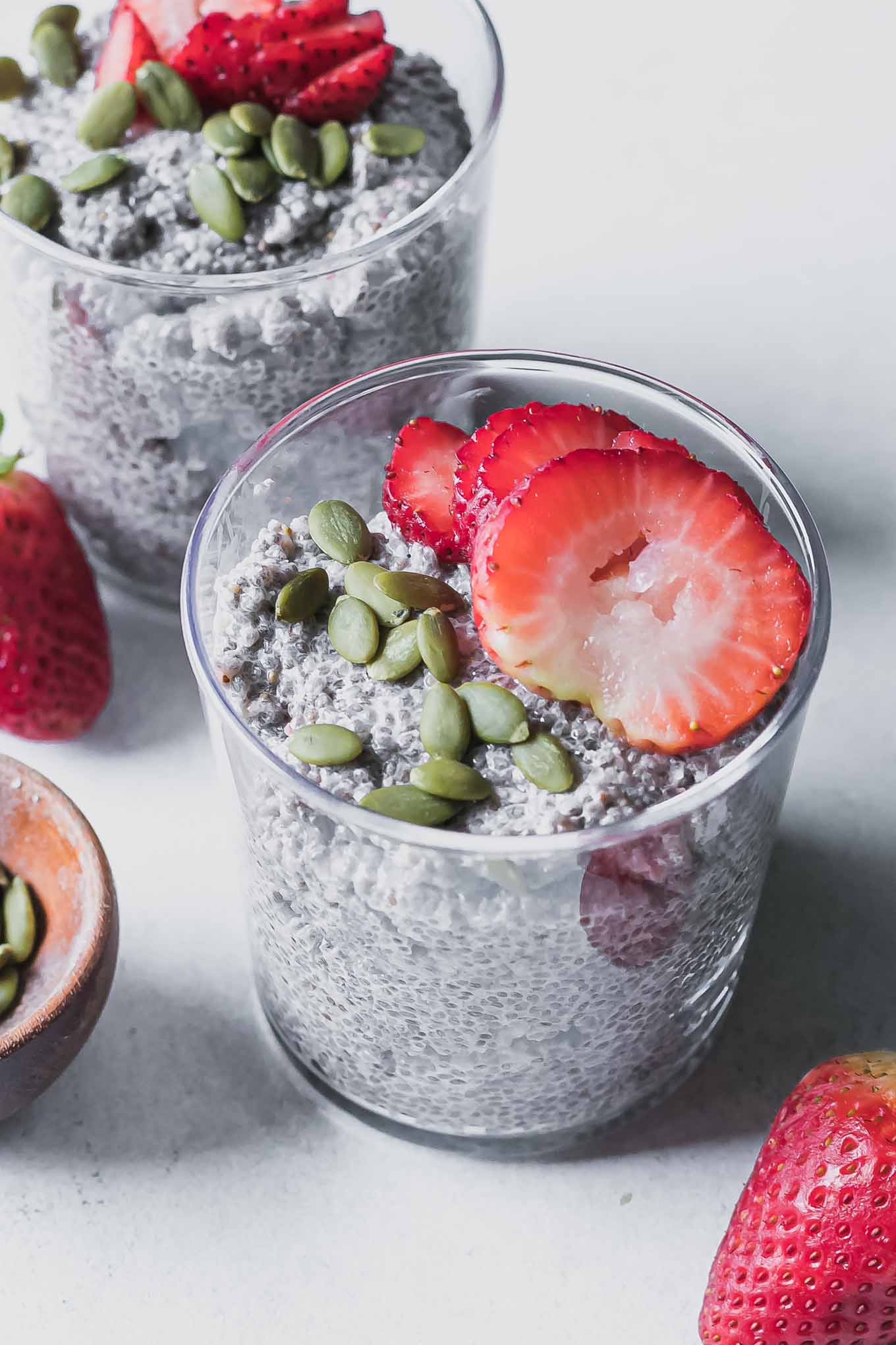 a glass with strawberry chia seed pudding and topped with a sliced strawberry on a white table with fresh strawberries