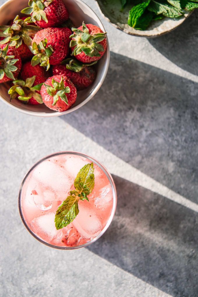 a pink mocktail on a table with a bowl of strawberries and mint