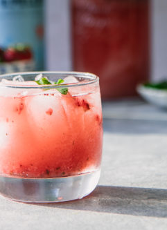 A glass of sparkling water with strawberries and mint on a blue table.