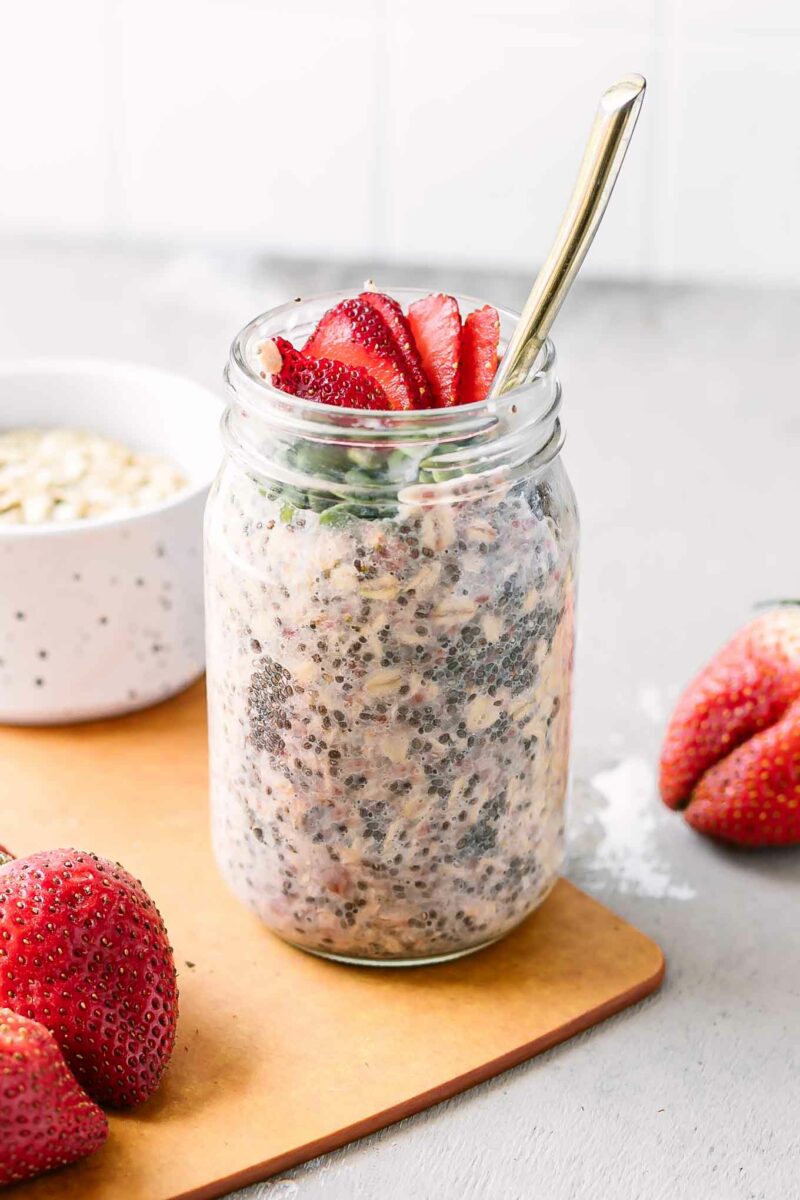 a jar of overnight oats with strawberries on a wood table with fresh strawberries