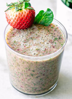 a glass with strawberry spinach smoothie with a strawberry garnish on a white table