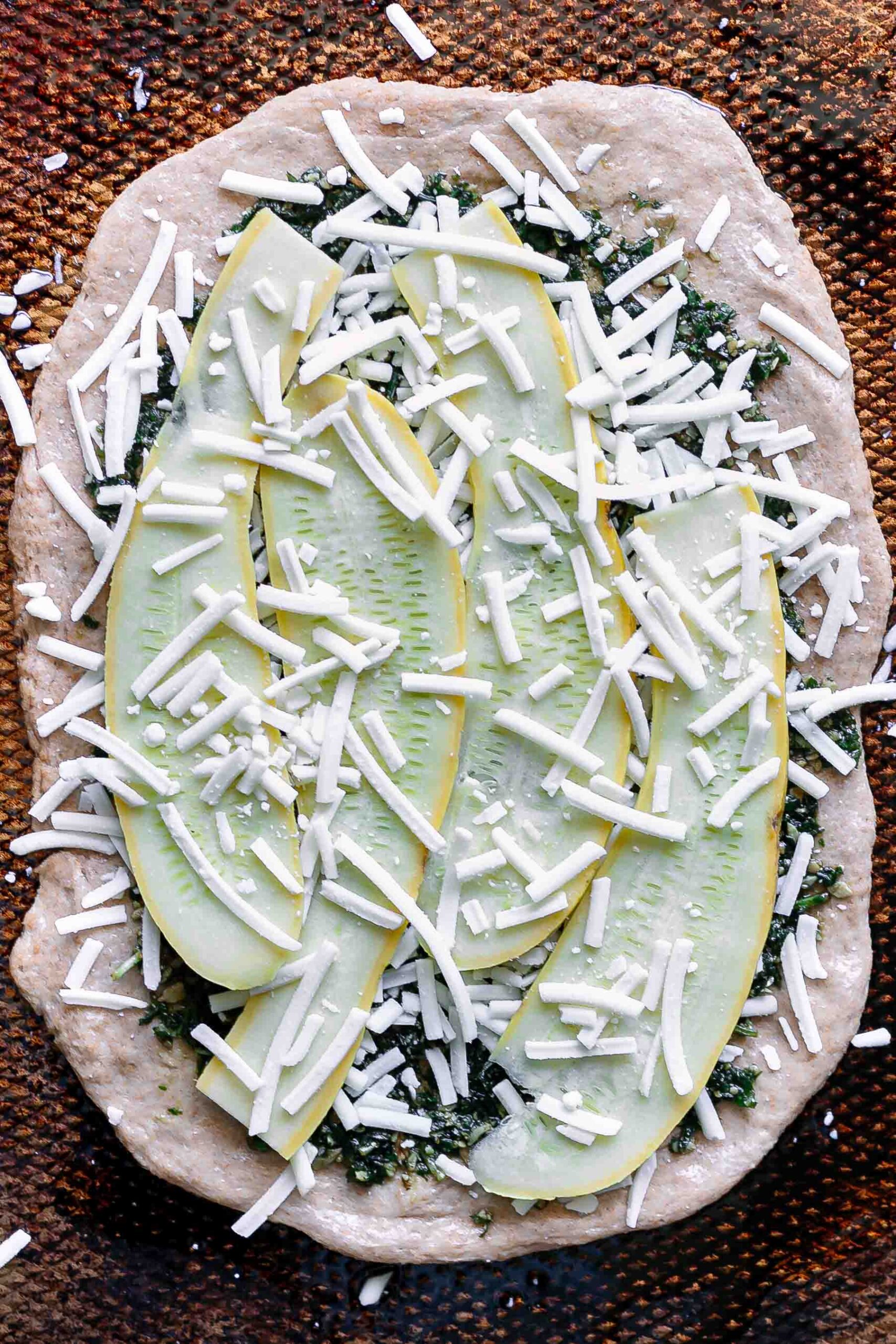 pizza dough topped with sunflower seed pesto, squash slices, and vegan cheese on a sheet pan before baking