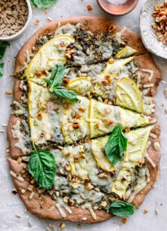 a pizza with yellow squash, pesto, corn, and basil on a white table