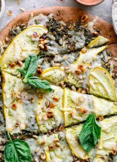 a pizza with sunflower seed pesto, sliced yellow summer squash, vegan cheese, a sprinkle of corn, and fresh basil on top