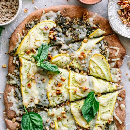 a pizza with sunflower seed pesto, sliced yellow summer squash, vegan cheese, a sprinkle of corn, and fresh basil on top