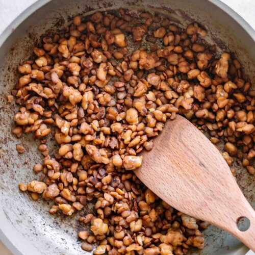 tempeh bacon bits in a pan after cooking with a wooden spoon