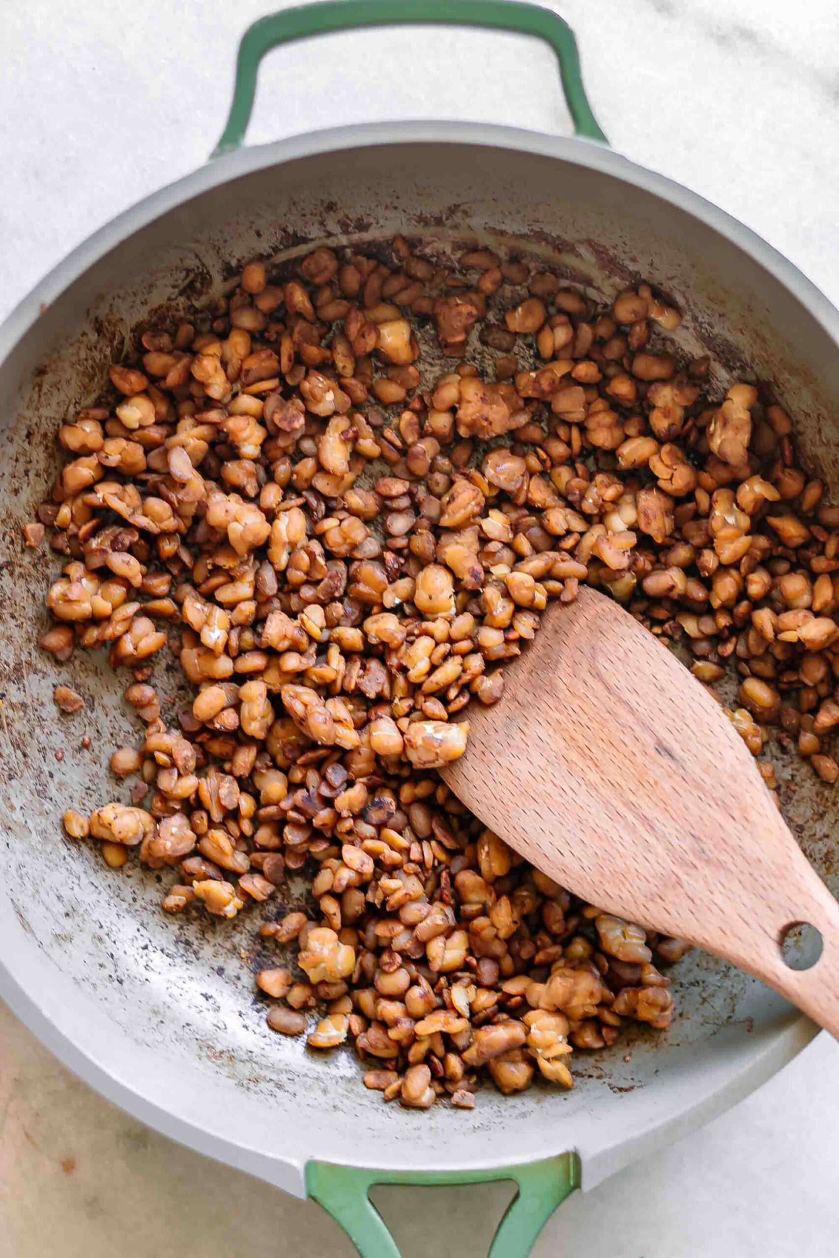 tempeh bacon bits in a pan after cooking with a wooden spoon
