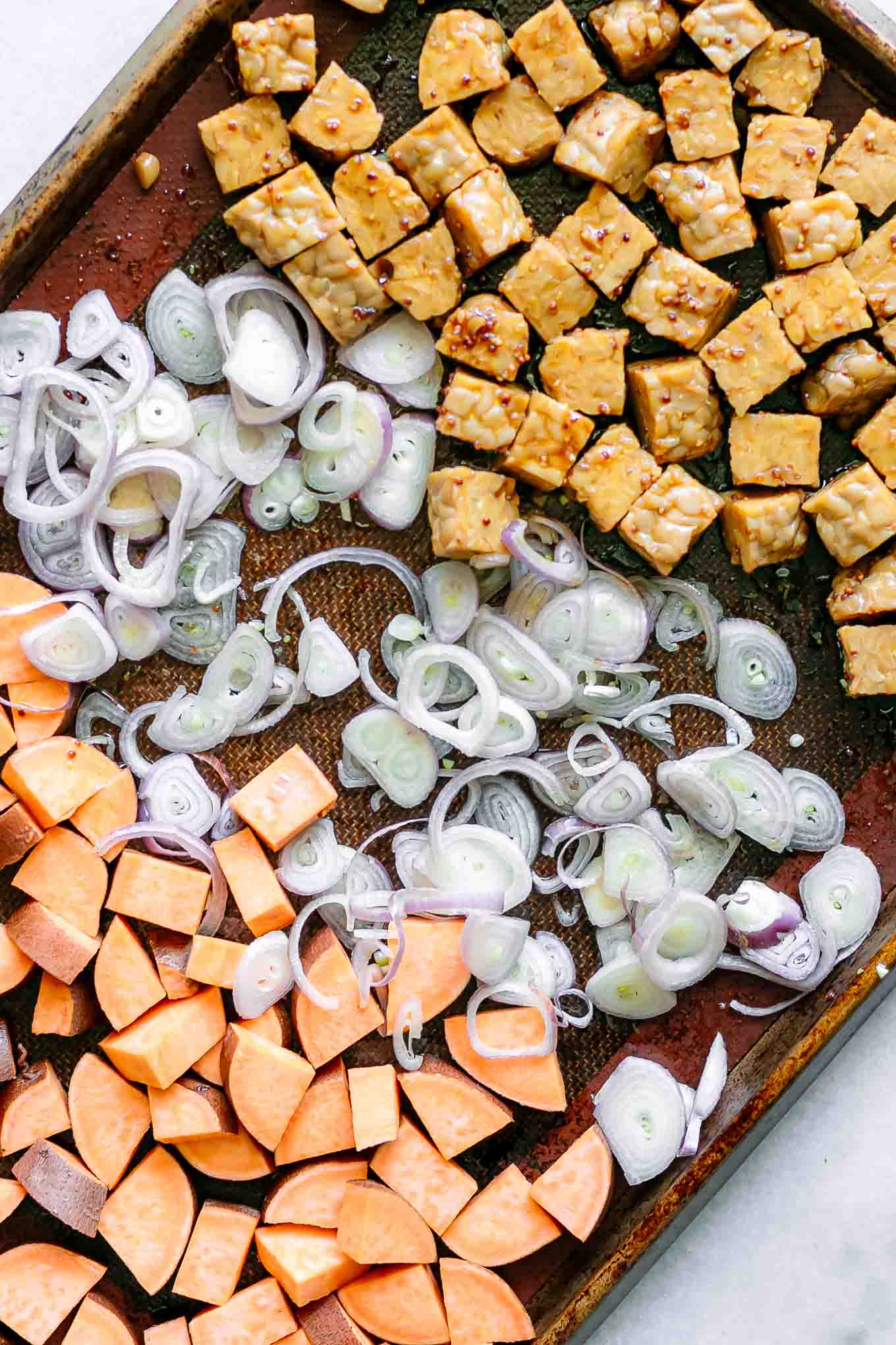 a sheet pan with sweet potatoes, tempeh, and shallots before roasting
