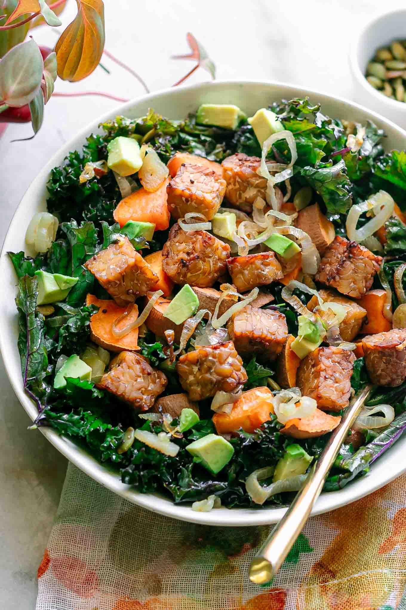 a bowl with quinoa, kale, sweet potatoes, tempeh, avocado, shallots, and pumpkin seeds