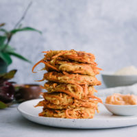 stacked vegetable cakes made of turnips and carrots on a white plate on a table with a plant in the background