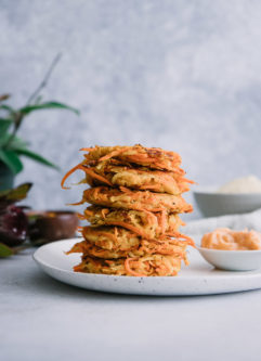 stacked vegetable cakes made of turnips and carrots on a white plate on a table with a plant in the background