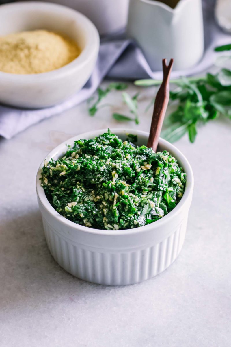 a small white ramekin of arugula pesto on a white table