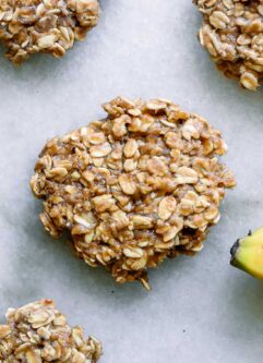 vegan banana oatmeal cookies on a white table with a yellow banana