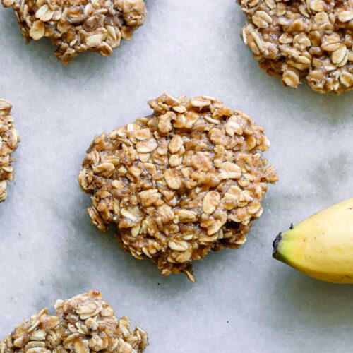 vegan banana oatmeal cookies on a white table with a yellow banana