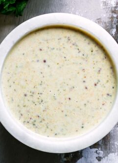 a white bowl with vegan caesar dressing on a wood table with a lemon and bowl of salt