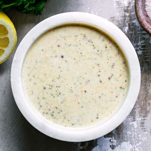 a white bowl with vegan caesar dressing on a wood table with a lemon and bowl of salt