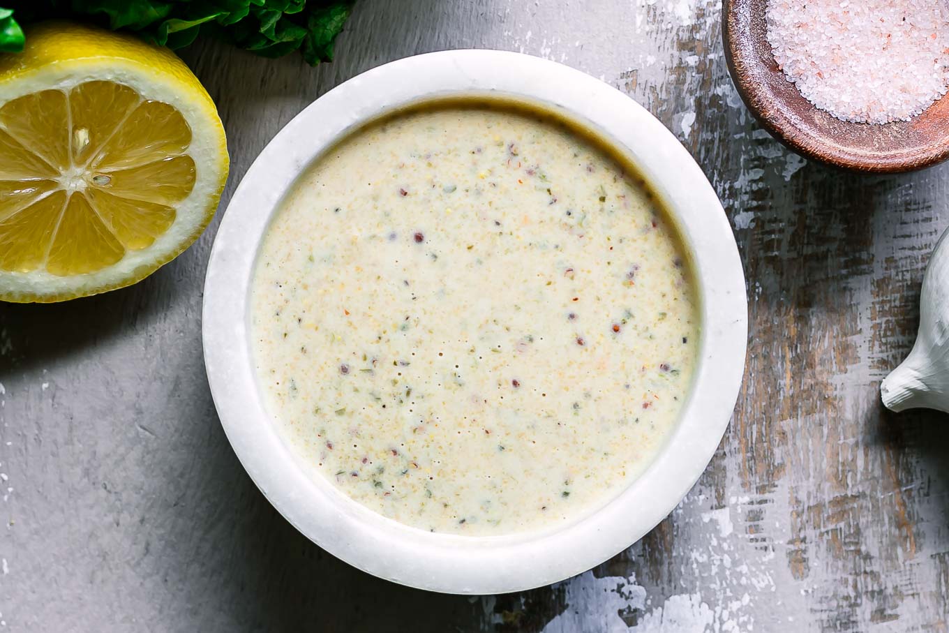 a white bowl with vegan caesar dressing on a wood table with a lemon and bowl of salt