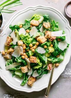 a vegan caesar salad on a white plate on a wood table
