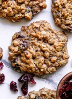 vegan cranberry oatmeal cookies on a white table with a bowl of dried cranberries