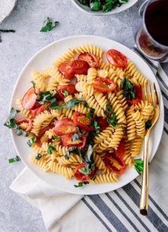 A white plate with Italian cold pasta salad with fusilli pasta, tomatoes, and basil with a gold fork.