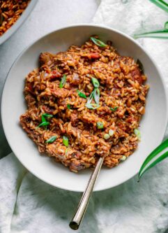 vegan jambalaya rice in a white bowl with a gold fork on white table