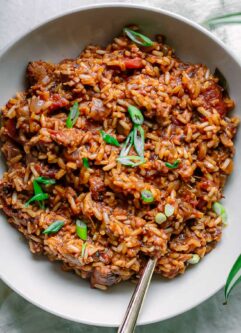 a bowl of vegan jambalaya on a white table garnishes with green onion slices