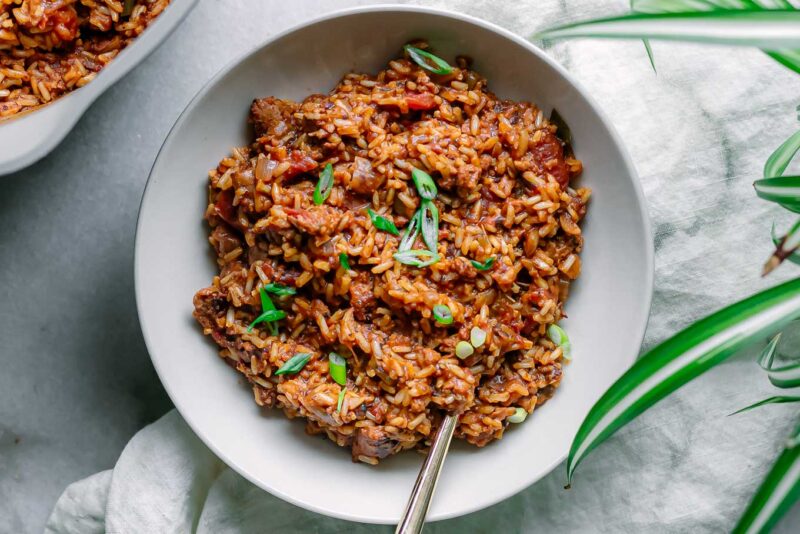 a bowl of vegan jambalaya on a white table garnishes with green onion slices