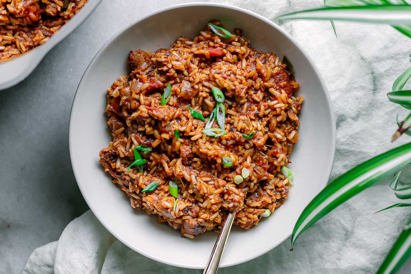 a bowl of vegan jambalaya on a white table garnishes with green onion slices