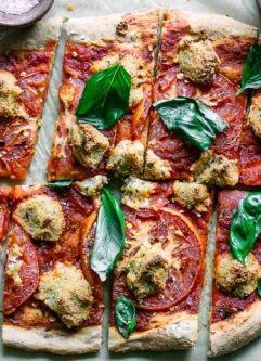 a vegan margherita pizza with sliced tomatoes, vegan mozzarella cheese, and fresh basil on a white table